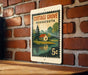 A metal sign with a vintage-style illustration of a cottage and a lake, mounted on a brick wall.