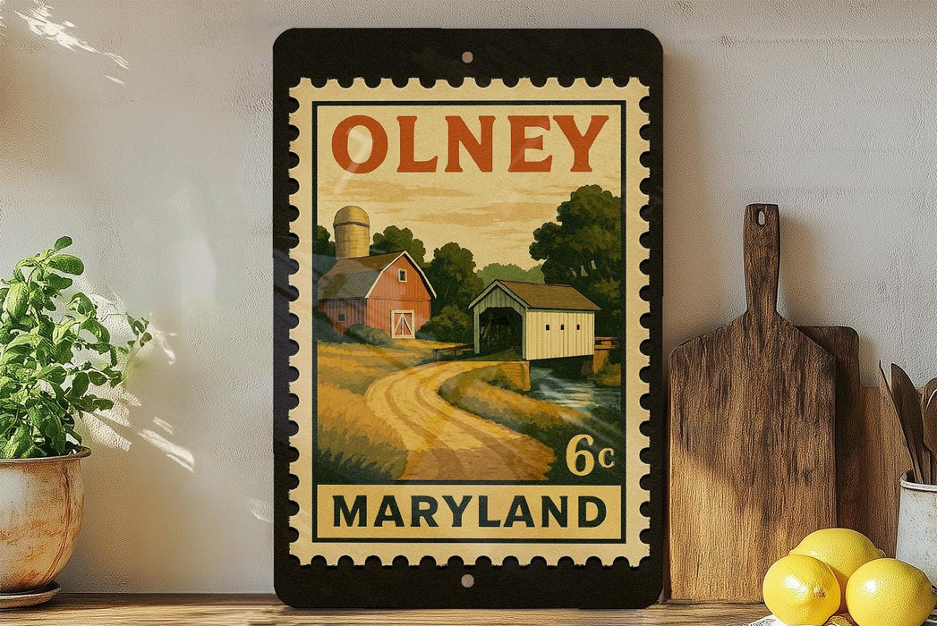 A framed vintage-style stamp depicting a rural scene in Maryland, with a barn, field, and stream. The stamp is placed on a shelf next to a wooden cutting board and a potted plant.