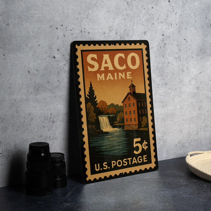 A vintage postage stamp from Maine, featuring a building and a waterfall, is displayed on a table.