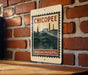 A vintage-style metal sign with the text "CHICOPEE" and "MASSACHUSETTS" printed on it, mounted on a brick wall.