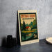 A vintage Minnesota postage stamp featuring a cottage and a lake, placed on a countertop next to some black camera lenses.