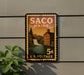 A vintage postage stamp from Maine, featuring a waterfall and a building, is displayed on a wall.