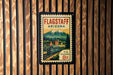 A vintage-style postage stamp from Flagstaff, Arizona, featuring a train and mountains in the background.