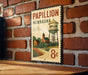 A vintage-style metal sign with the text "PAPILLON NEBRASKA" and an illustration of a water tower, mounted on a brick wall.