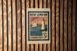 A New London postage stamp from Connecticut, featuring a lighthouse and a ship, is displayed on a wooden wall.