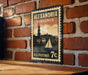 A vintage-style postage stamp from the United States, featuring a sailboat and a cityscape, is displayed on a brick wall.