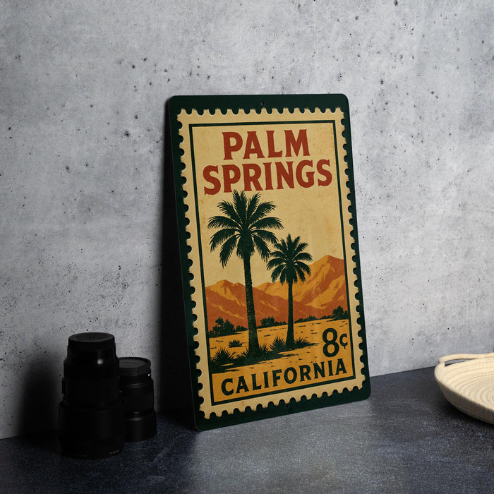 A vintage-style metal sign for Palm Springs, California, featuring palm trees and mountains, is displayed on a table.