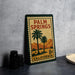 A vintage-style metal sign for Palm Springs, California, featuring palm trees and mountains, is displayed on a table.