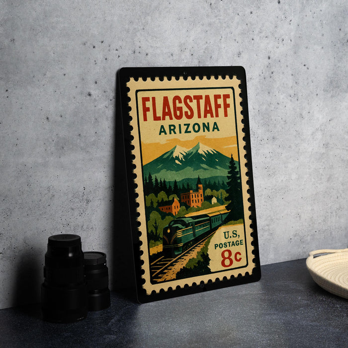 A vintage-style postage stamp from Flagstaff, Arizona, featuring a train and mountains, placed on a countertop next to some camera equipment.