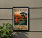 A vintage-style sign for San Mateo, California, featuring a bridge and a sunset landscape.