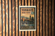 A vintage postage stamp from the United States of America, featuring an illustration of a cityscape and a clock tower, mounted on a wooden wall.