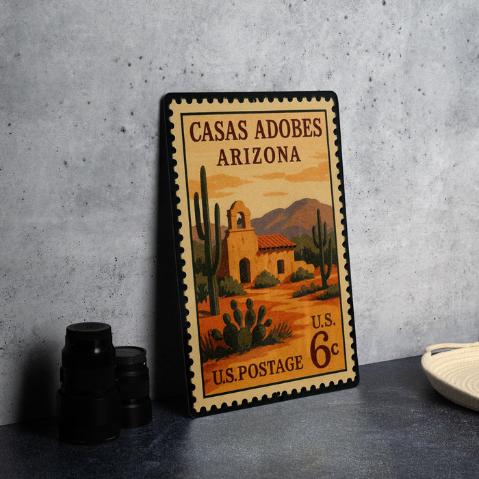 A vintage U.S. postage stamp depicting a desert scene with a building and cacti, placed on a countertop next to some black camera lenses.
