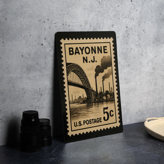 A Bayonne New Jersey postage stamp is displayed on a table, featuring an illustration of a bridge and steam pipes.