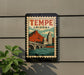 A vintage-style poster of Tempe, Arizona, featuring a mountain, bridge, and buildings, is displayed on a wall.