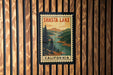 A vintage-style postage stamp depicting Shasta Lake, with the text "SHasta Lake" and "California" printed on it, is displayed on a wooden wall.