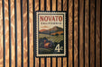 A vintage-style postage stamp from Novato, California, featuring a rural landscape with a farmhouse and mountains in the background.