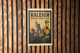 A vintage postage stamp from Raleigh, North Carolina, featuring a cityscape with tall buildings and a fountain.