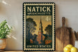 A vintage-style postage stamp from Massachusetts, featuring a church steeple and a small town scene, is displayed on a shelf next to a wooden cutting board and some lemons.