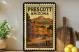 A framed vintage postage stamp from Prescott, Arizona, depicting a street scene with buildings and mountains in the background.