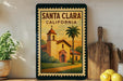 A framed poster of Santa Clara, California, featuring a church and palm trees, is displayed on a wall next to a wooden cutting board and a potted plant.