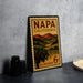 A vintage Napa California postage stamp is displayed on a table, featuring a scenic countryside landscape with vineyards and mountains.