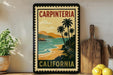 A vintage-style poster of Carpinteria, California, featuring palm trees, a beach, and mountains, is displayed on a wall next to a wooden cutting board and a potted plant.