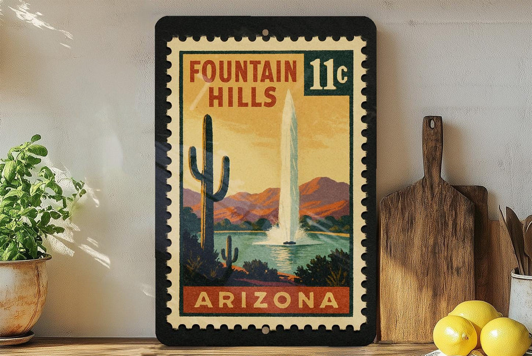 A framed vintage postage stamp depicting a desert landscape with a fountain, surrounded by various kitchen utensils and a potted plant.