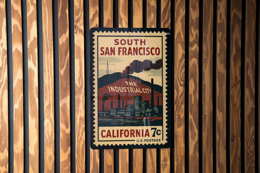 A vintage-style postage stamp from California, featuring an illustration of a city skyline and industrial buildings, mounted on a wooden wall.