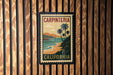 A vintage-style poster of Carpinteria, California, featuring palm trees and a beach landscape, is displayed on a wooden wall.