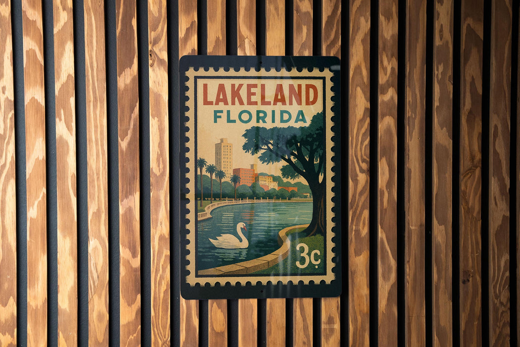 A vintage-style postage stamp from Lakeland, Florida, featuring a serene lake, palm trees, and a swan, is displayed on a wooden wall.