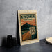 A metal sign with a vintage-style illustration of Route 66 in Arizona, featuring mountains and a road.