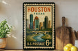 A framed vintage postage stamp from the United States Postal Service, featuring an illustration of the Houston skyline and a river, is displayed on a shelf next to a wooden cutting board and some lemons.