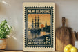 A vintage-style postage stamp from New Bedford, Massachusetts, featuring a sailing ship on a body of water with a sunset in the background.