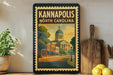 A framed poster of the Kannapolis North Carolina landmark, featuring a building with a dome and a street scene, is displayed on a shelf next to a wooden cutting board and a potted plant.