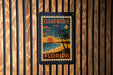 A vintage-style postage stamp from Florida, featuring a beach scene with palm trees and a sunset, is displayed on a wooden wall.