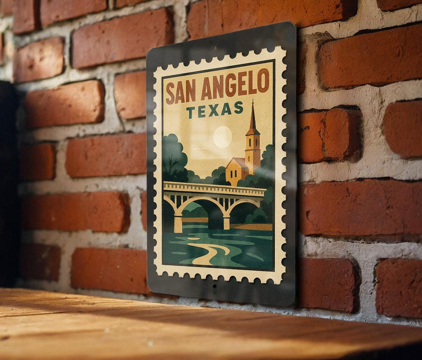 A vintage-style metal stamp with the text "SAN ANGELO TEXAS" and an illustration of a bridge and a church, hanging on a brick wall.