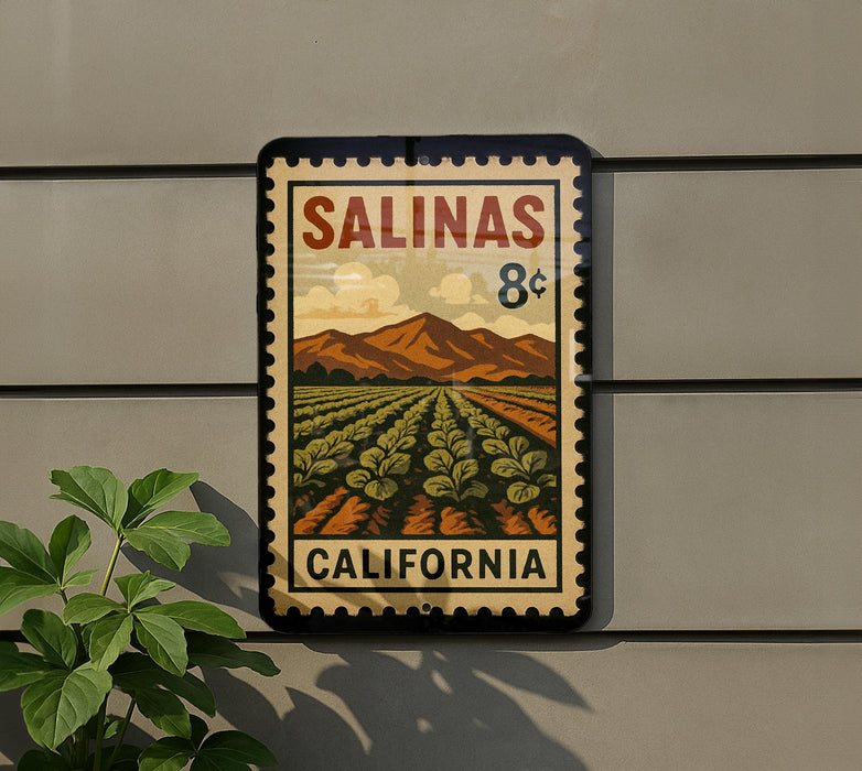 A vintage-style postage stamp depicting a field of crops, with mountains in the background, mounted on a wall.