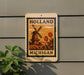A sign with the text "HOLAND MICHIGAN" and an illustration of a windmill and tulips, mounted on a wall.