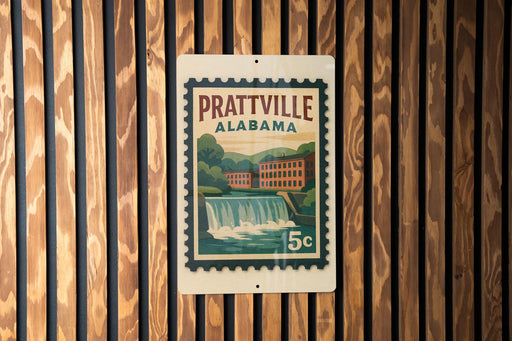 A vintage postage stamp from Prattville, Alabama, featuring a waterfall and buildings, is displayed on a wooden wall.
