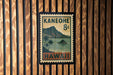 A vintage-style postage stamp from Hawaii, featuring a mountain landscape and palm trees, is displayed on a wooden wall.