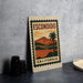 a vintage-style metal sign with a palm tree and a landscape, placed on a countertop next to some black camera lenses.
