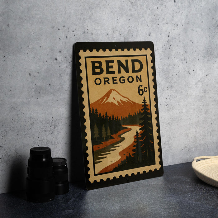 A metal sign with a vintage design depicting a mountain landscape and a river, along with the text "BEND OREGON 6c".