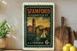 A vintage postage stamp from the United States of America, featuring a cityscape with a sailboat on the water, displayed on a shelf next to a wooden cutting board and some potted plants.
