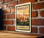 A vintage-style metal stamp depicting the Berkeley skyline, with a clock tower and surrounding buildings, is mounted on a brick wall.
