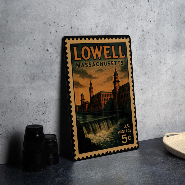 A vintage postage stamp from Lowell, Massachusetts, featuring a cityscape with a waterfall, placed on a table next to some black camera lenses.