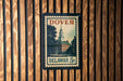 A vintage Dover 5c postage stamp featuring a building with a clock tower, mounted on a wooden wall.