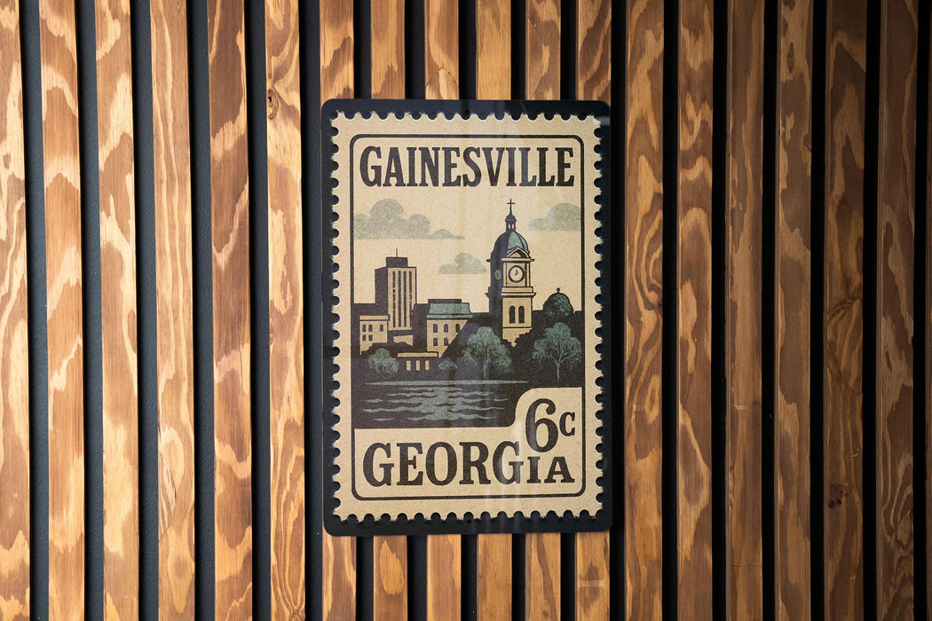 A vintage-style postage stamp from Gainesville, Georgia, featuring a cityscape and a clock tower.