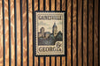 A vintage-style postage stamp from Gainesville, Georgia, featuring a cityscape and a clock tower.