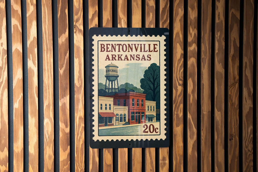 A vintage postage stamp from Bentonville, Arkansas, featuring a water tower and buildings, is displayed on a wooden wall.