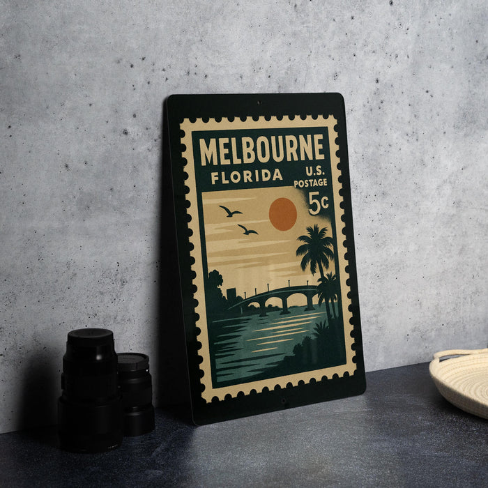 A vintage postage stamp from Melbourne, Florida, featuring a sunset and palm trees, is displayed on a table.